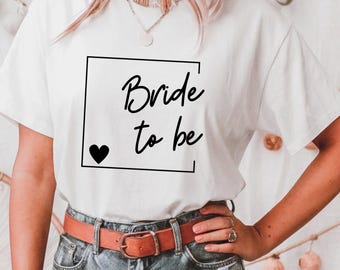 Puede incluir: Camiseta blanca con un marco cuadrado negro alrededor del texto "Bride to be" y un pequeño corazón negro.
