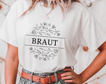 May include: White t-shirt with a floral design and the word "BRAUT" printed on it.