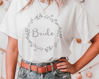 Puede incluir: Camiseta blanca con un diseño de corona de flores y la palabra "Bride" en el centro.