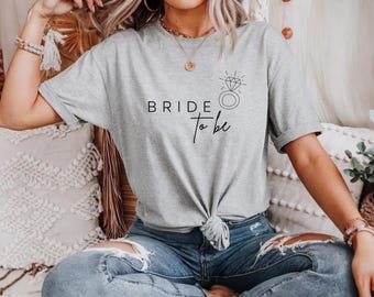 May include: A gray t-shirt with the text "BRIDE to be" and a simple line drawing of a diamond ring.