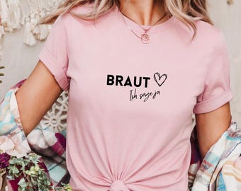 Puede incluir: Camiseta rosa con el texto "BRAUT Ich sage ja" y un corazón.