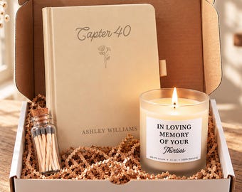 May include: A gift box containing a cream-coloured journal with the text "Capter 40" and "ASHLEY WILLIAMS" printed on the cover, a small glass bottle filled with matches, and a lit candle with a label reading "IN LOVING MEMORY OF YOUR Thirties".