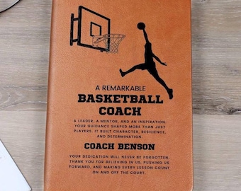May include: A brown leather notebook with a basketball design. The cover shows a basketball hoop and a player silhouette. Text reads "A Remarkable Basketball Coach" and includes a personalized message.