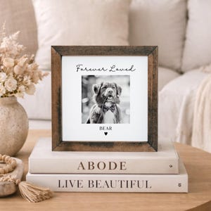 Puede incluir: Un marco de fotos cuadrado de madera con una imagen en blanco y negro de un perro con pajarita. El texto "Forever Loved" est&aacute; encima de la foto, con el nombre "BEAR" y un coraz&oacute;n debajo. El marco est&aacute; sobre dos libros.