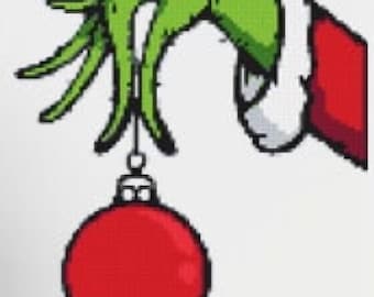 May include: A pixelated illustration of a green hand, wearing a red and white sleeve, holding a red Christmas ornament. The hand is reaching down to hold the ornament, which is hanging from a silver hook. The image is on a white background.