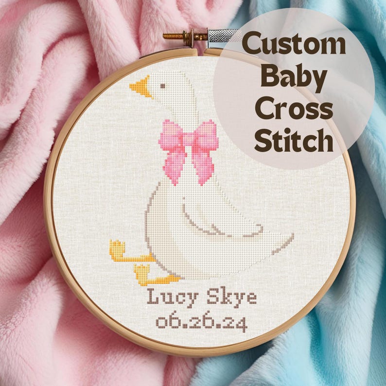 May include: A white goose cross stitch pattern with a pink bow, personalized with the name "Lucy Skye" and the date "06.26.24".
