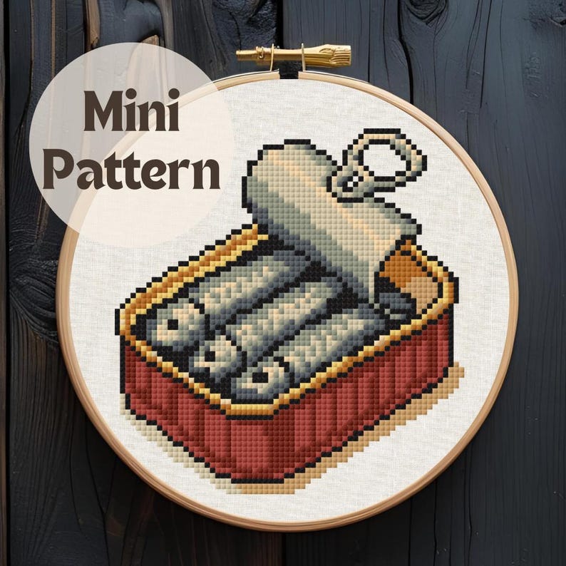 May include: Cross-stitch pattern of a sardine can, featuring a red and gold container with silver fish. The design is set in a wooden embroidery hoop. The words "Mini Pattern" are in a circle above the design.