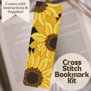 May include: A cross stitch bookmark kit featuring a sunflower design. The bookmark has a yellow and brown color scheme, with the text "Cross Stitch Bookmark Kit" on a white circle. The image also includes the text "Comes with Instructions & Supplies!"