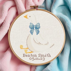 May include: White embroidered goose with a blue bow, sitting on a white background. The text "Benton Smith 05.11.23" is below the goose.
