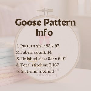 May include: A white embroidery hoop with the text "Goose Pattern Info" in brown text. The hoop contains information about the pattern size, fabric count, finished size, total stitches, and the method used for stitching. The text reads: "1. Pattern size: 83 x 97", "2. Fabric count: 14", "3. Finished size: 5.9 x 6.9"", "4. Total stitches: 3,167", "5. 2 strand method".