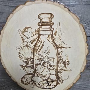 May include: A wood-burned art piece featuring a glass bottle filled with seashells and starfish. The bottle is surrounded by various seashells and starfish, all etched into a round wooden slice. The artwork is a natural wood color.