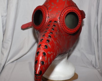 Pode incluir: Uma máscara de médico da peste de couro vermelho com detalhes pretos e um padrão floral. A máscara tem dois grandes olhos redondos e um bico longo.