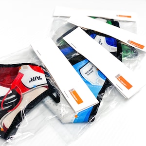 May include: Four face masks in individual plastic packaging. The masks feature different designs of sneakers, including a red and white Air Jordan design, a blue and white design, a blue and green design, and a green and black design. Each package has a white label with the text "Facemask" and a barcode.