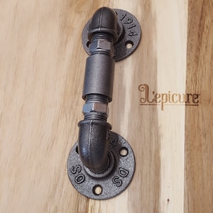 Peut inclure: Une poignée de porte en métal noir avec deux brides. Les brides sont marquées du texte "DSS" et "1914".