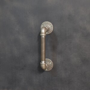 May include: A black metal door handle with a pipe design. The handle has a round base and a curved pipe extending upwards.