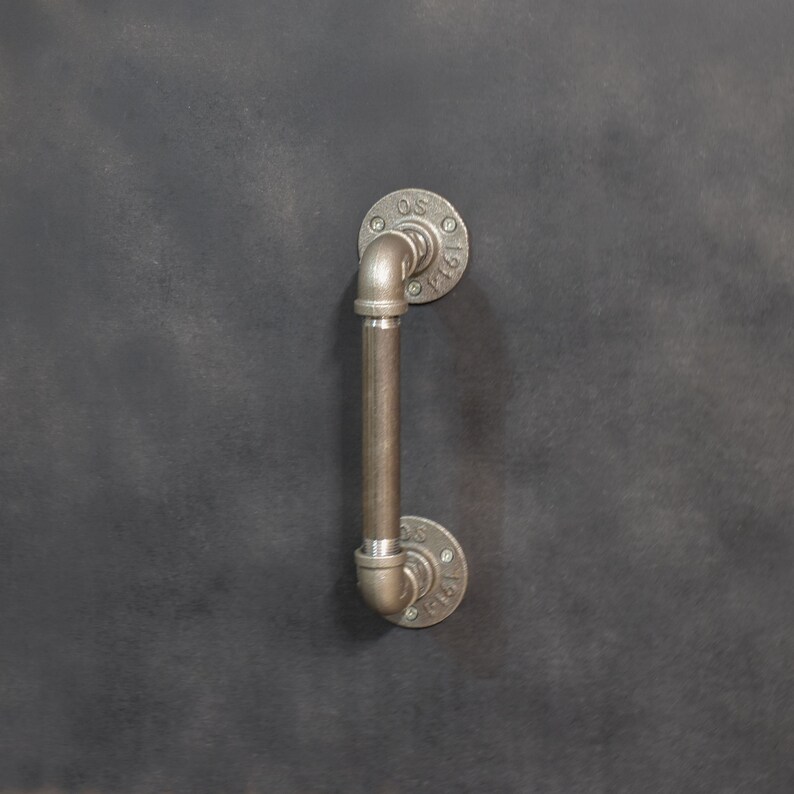 May include: A black metal door handle with a pipe design. The handle has a round base and a curved pipe extending upwards.