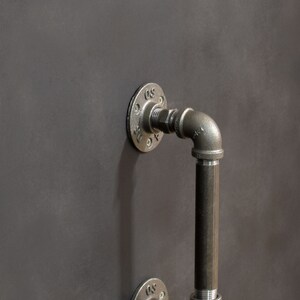 May include: A black metal pipe door handle with a round flange. The handle is attached to a wall.