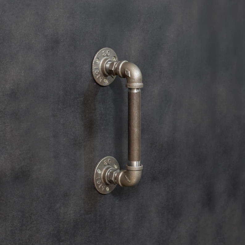 May include: A black metal door handle with a pipe design. The handle is attached to a wall with two round flanges.