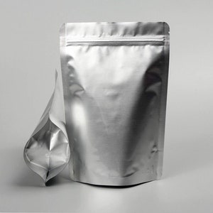 May include: A silver stand-up pouch with a zipper closure. The pouch is made of a shiny, metallic material and is empty.