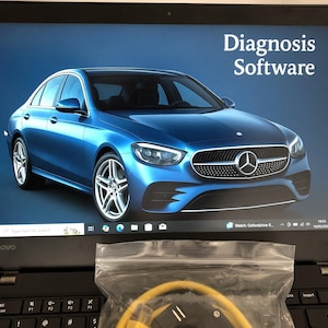 May include: A black Lenovo laptop showing "Diagnosis Software" on the screen, with a blue Mercedes-Benz car image. A clear bag with a yellow cable is in front of the laptop.