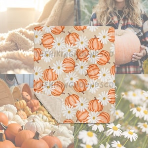 May include: A beige throw blanket featuring a pattern of orange pumpkins and white daisies. The blanket has a soft, plush texture on the underside. The design evokes a fall or autumn theme, perfect for seasonal decor.