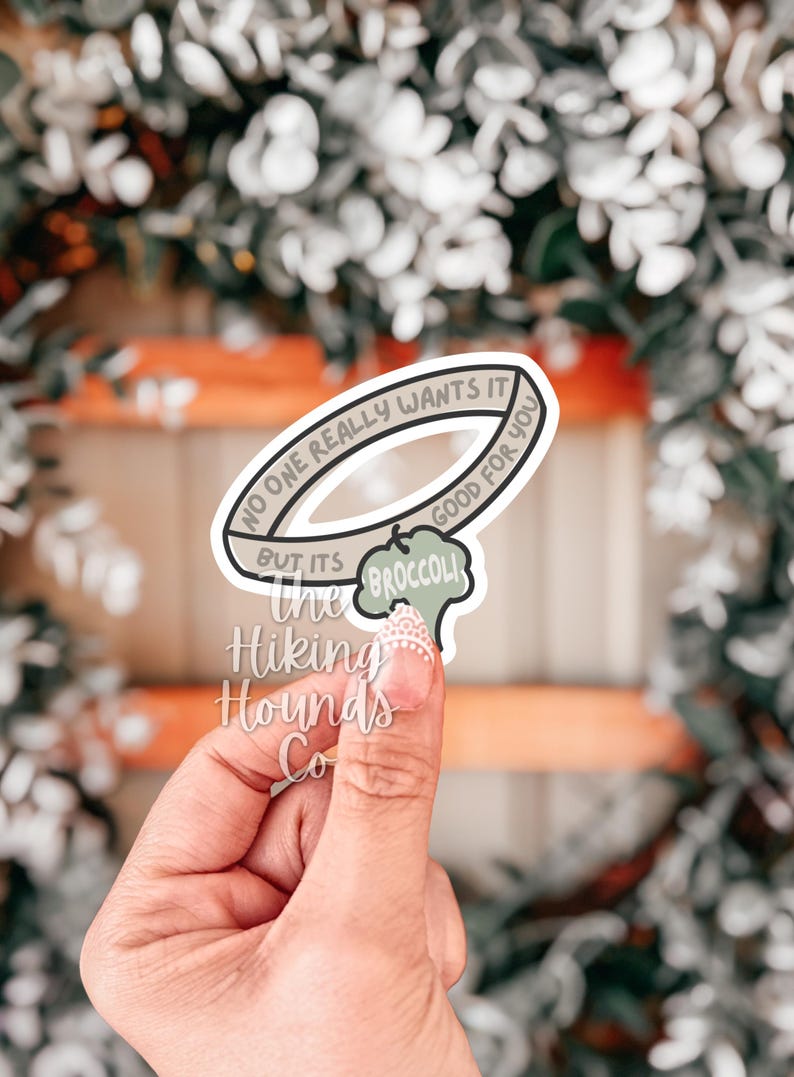 May include: A sticker with the text "NO ONE REALLY WANTS IT BUT ITS GOOD FOR YOU" in a circular design. A broccoli graphic is below the text. The sticker also has the text "the BROCCOLI" and "Hiking Hounds Co."