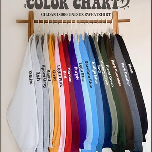 May include: A color chart of Gildan 18000 unisex sweatshirts in various colors, including white, ash, sport grey, sand, gold, light pink, red, maroon, purple, light blue, carolina blue, indigo blue, navy, military green, forest green, dark chocolate, dark heather, and black.
