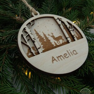Pu&ograve; includere: Un ornamento natalizio in legno con un design di cervo e alberi. L'ornamento &egrave; personalizzato con il nome "Amelia".