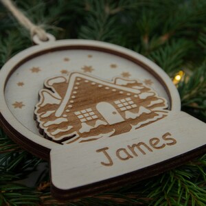 Pu&ograve; includere: Un ornamento natalizio in legno a forma di sfera di neve con una casetta di pan di zenzero all'interno. L'ornamento &egrave; personalizzato con il nome "James".