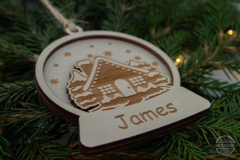 Pu&ograve; includere: Un ornamento natalizio in legno a forma di sfera di neve con una casetta di pan di zenzero all'interno. L'ornamento &egrave; personalizzato con il nome "James".