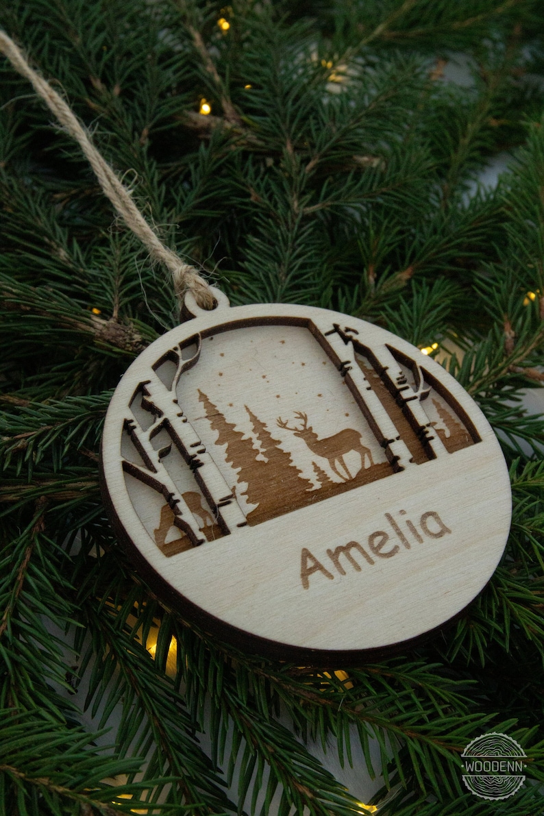 Pu&ograve; includere: Un ornamento natalizio in legno con un design di cervo e alberi. L'ornamento &egrave; personalizzato con il nome "Amelia".
