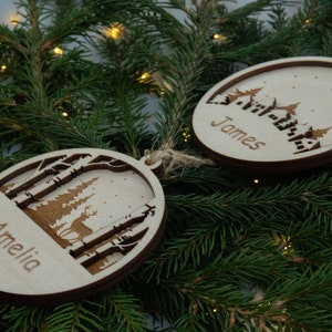 Pu&ograve; includere: Due decorazioni natalizie in legno con un design a tema invernale. Un ornamento ha il nome "Amelia" e l'altro il nome "James".