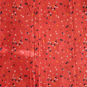 May include: Red fabric with a scattered star pattern in white, blue, and yellow. The fabric has a light blue border with the word "POP!" and other text. This fabric is suitable for various sewing and crafting projects.