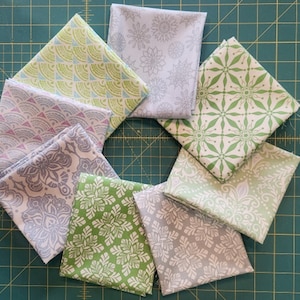 May include: Eight fabric squares with different patterns in shades of green and gray. The patterns include geometric shapes, floral designs, and abstract motifs.