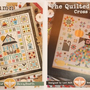 May include: Two cross stitch patterns featuring autumn themes. The first pattern is called "Autumn Love" and features a house with a "Home" sign and the word "Autumn" in a quilt block design. The second pattern is called "The Quilted Witch" and features a witch with a broom and a pumpkin in a quilt block design.