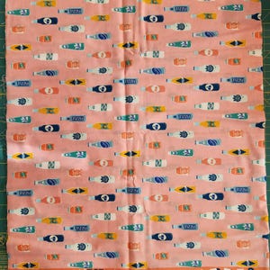 May include: Pink fabric with a repeating pattern of colorful soda bottles. The bottles are in various colors, including blue, yellow, and white, with the word "FIZZLE" printed on them. The fabric has the text "POP!" and "RASHIDA COLEMAN HALE" printed on the bottom.