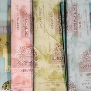 May include: A collection of six fabric swatches with a vintage, distressed look. The fabric features a repeating pattern of text and images, including the words "Josef March" and "Bressanone".