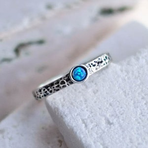 May include: A silver ring with a textured band and a small blue opal gemstone.
