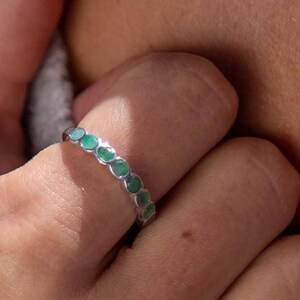 Könnte beinhalten: Ein silberner Ring mit einer Reihe grüner ovaler Steine. Der Ring befindet sich an einem Finger.