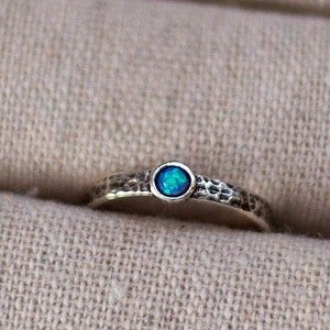 May include: A silver ring with a blue opal gemstone set in the center. The band of the ring has a hammered texture.