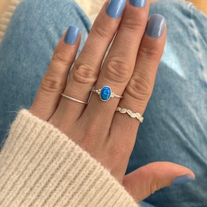 May include: A silver ring featuring a blue oval opal gemstone. The ring is worn on a finger with blue nail polish.