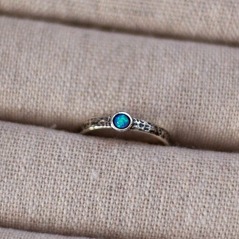 May include: A silver ring with a blue opal gemstone set in the center. The band of the ring has a hammered texture.