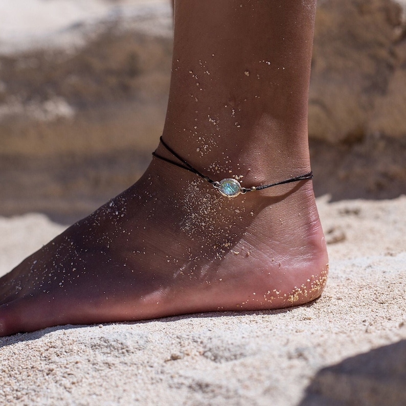 May include: A simple anklet with a small, oval-shaped turquoise gemstone charm on a black cord.