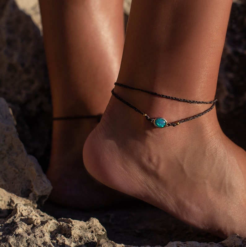 May include: A black ankle bracelet with a turquoise gemstone charm. The bracelet is made of thin cord and has a simple design.