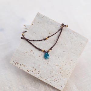 May include: A brown cord bracelet with gold beads and a blue gemstone pendant.