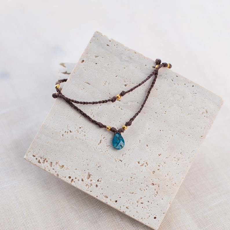 May include: A brown cord bracelet with gold beads and a blue gemstone pendant.