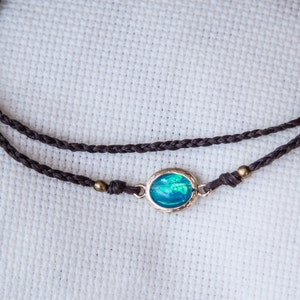 May include: A brown braided cord necklace with a silver oval pendant featuring a blue opal gemstone.