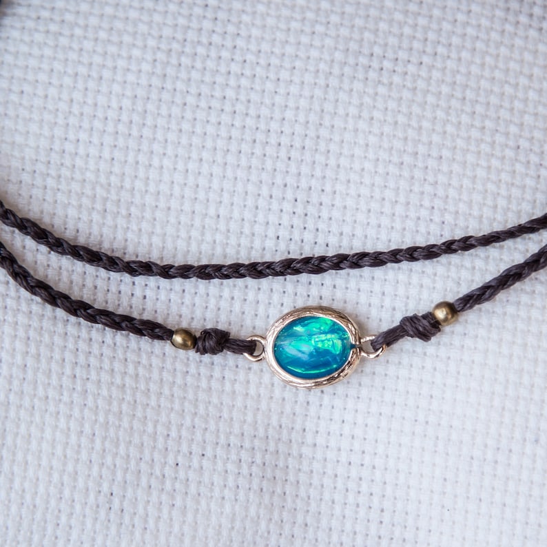 May include: A brown braided cord necklace with a silver oval pendant featuring a blue opal gemstone.