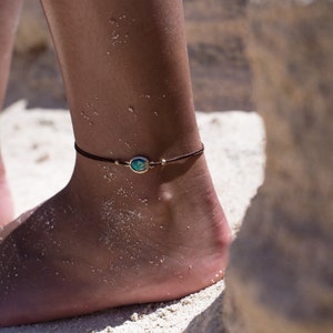 May include: A brown ankle bracelet with a small, round, green and blue gemstone charm.