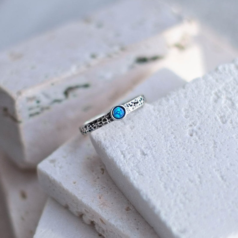 May include: A silver ring with a textured band and a small blue opal gemstone.